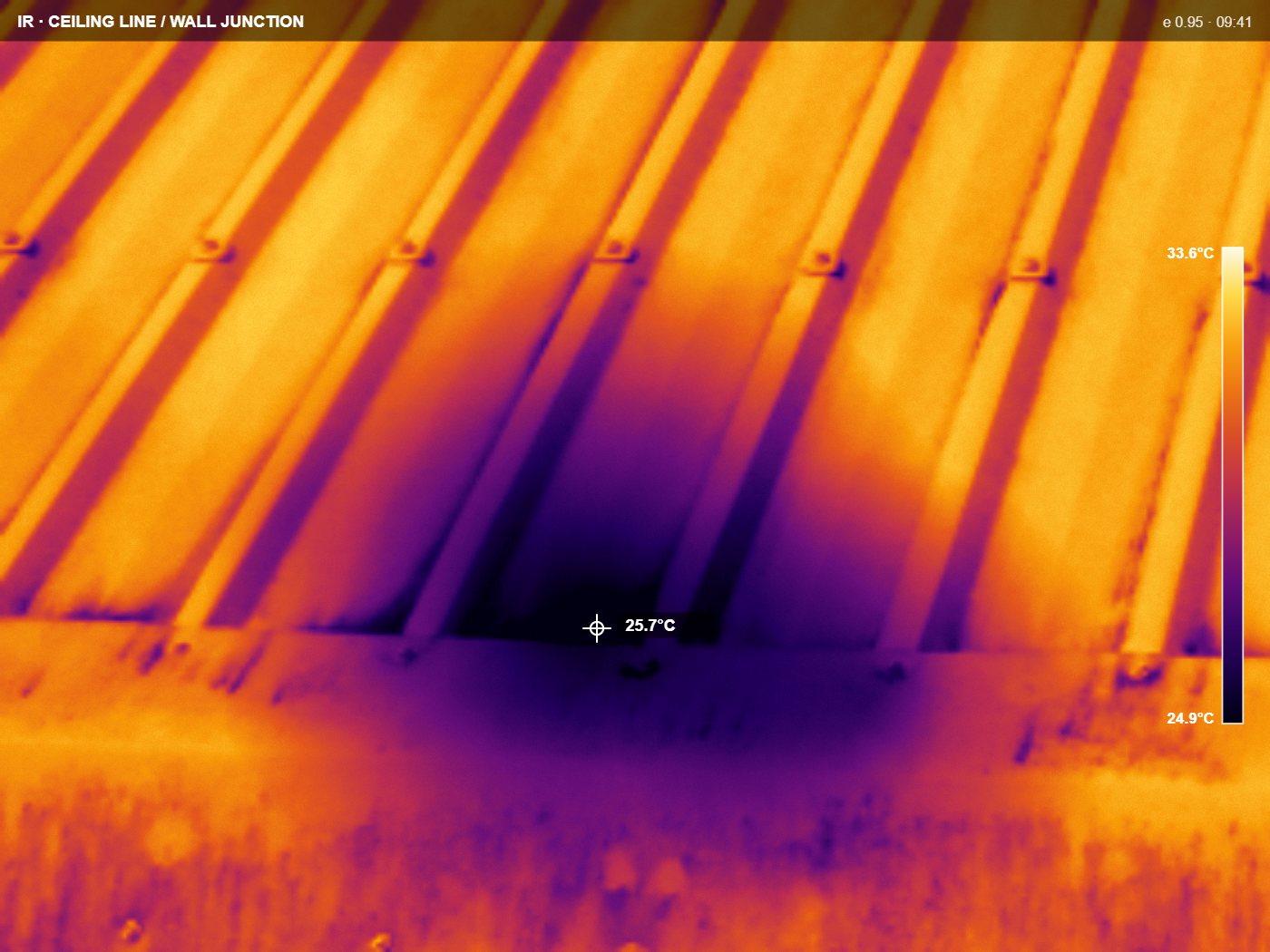 Thermal frame at a ceiling line and wall junction, ironbow palette, cooler band along the junction with a temperature scale